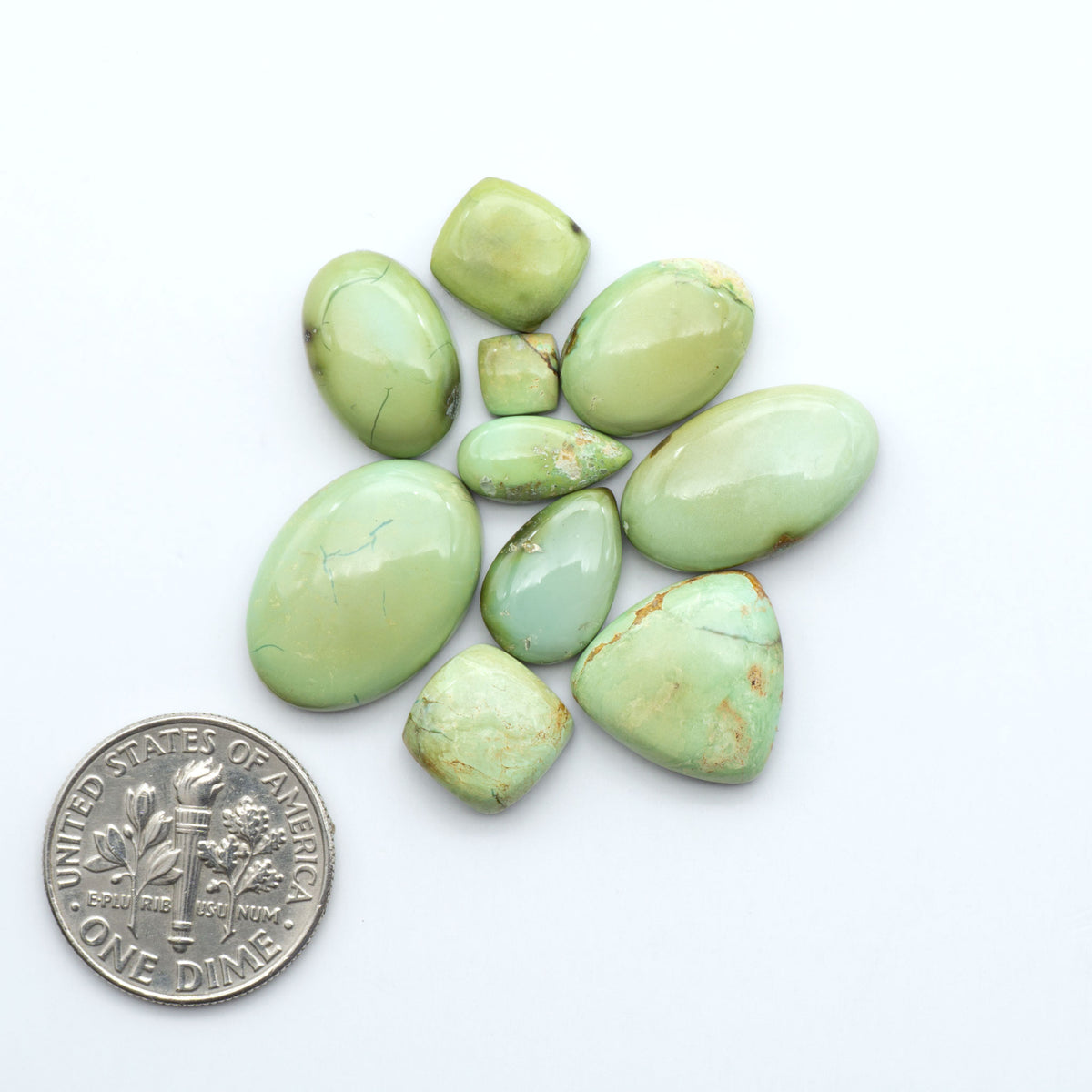 Sonoran Mountain Turquoise cabochons, blue-green color with natural matrix, polished stones on a white background, with a US dime for scale