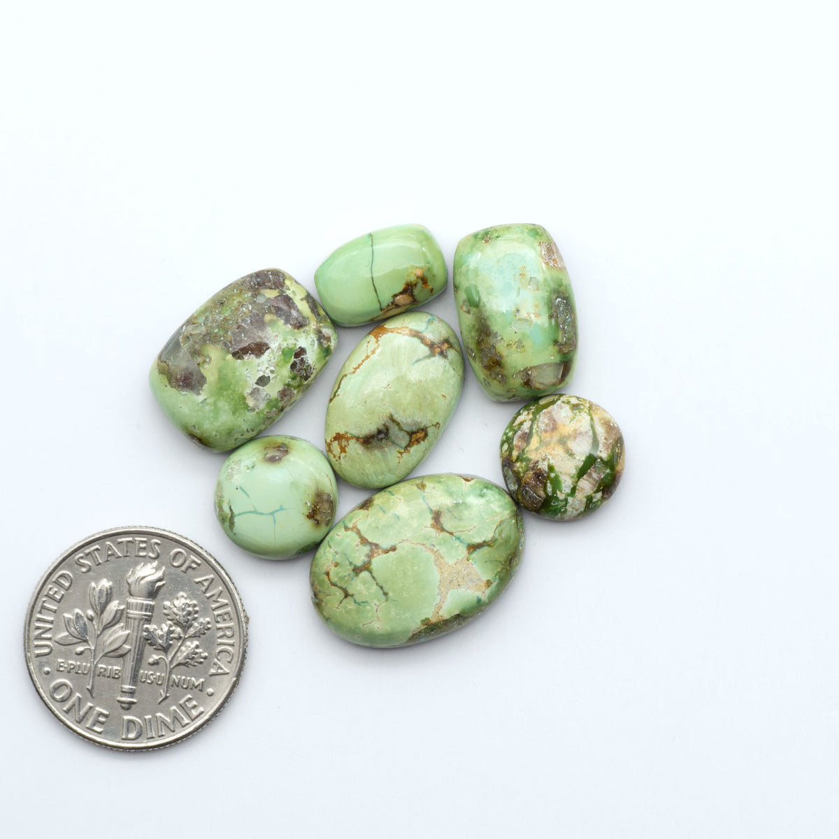 Sonoran Mountain Turquoise cabochons, blue-green color with natural matrix, polished stones on a white background, with a US dime for scale