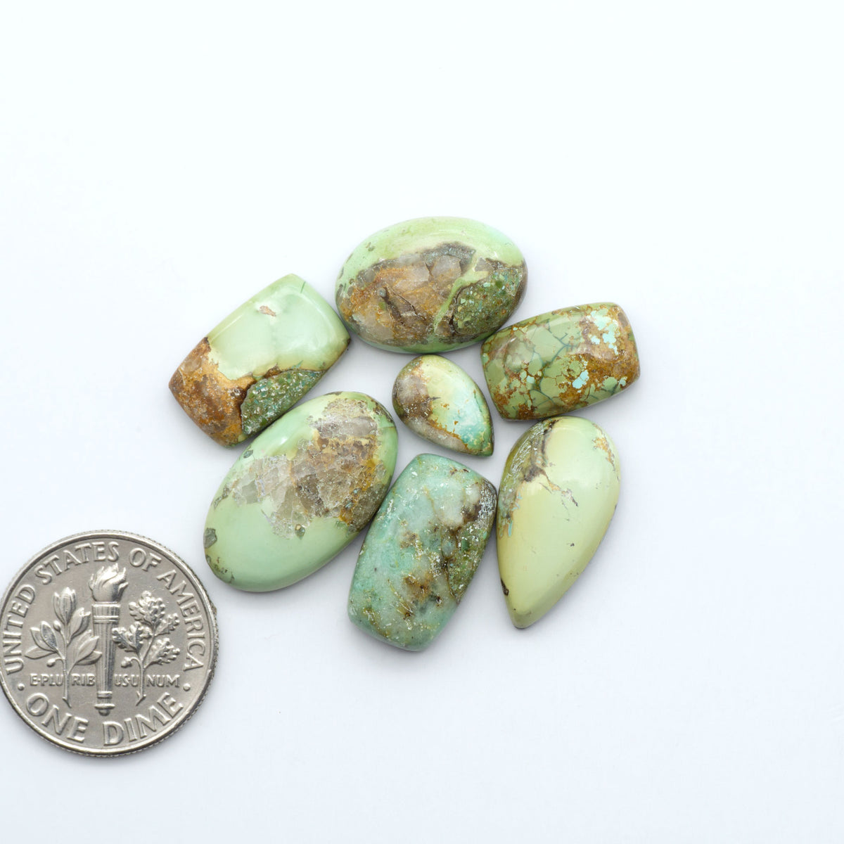 Sonoran Mountain Turquoise cabochons, blue-green color with natural matrix, polished stones on a white background, with a US dime for scale