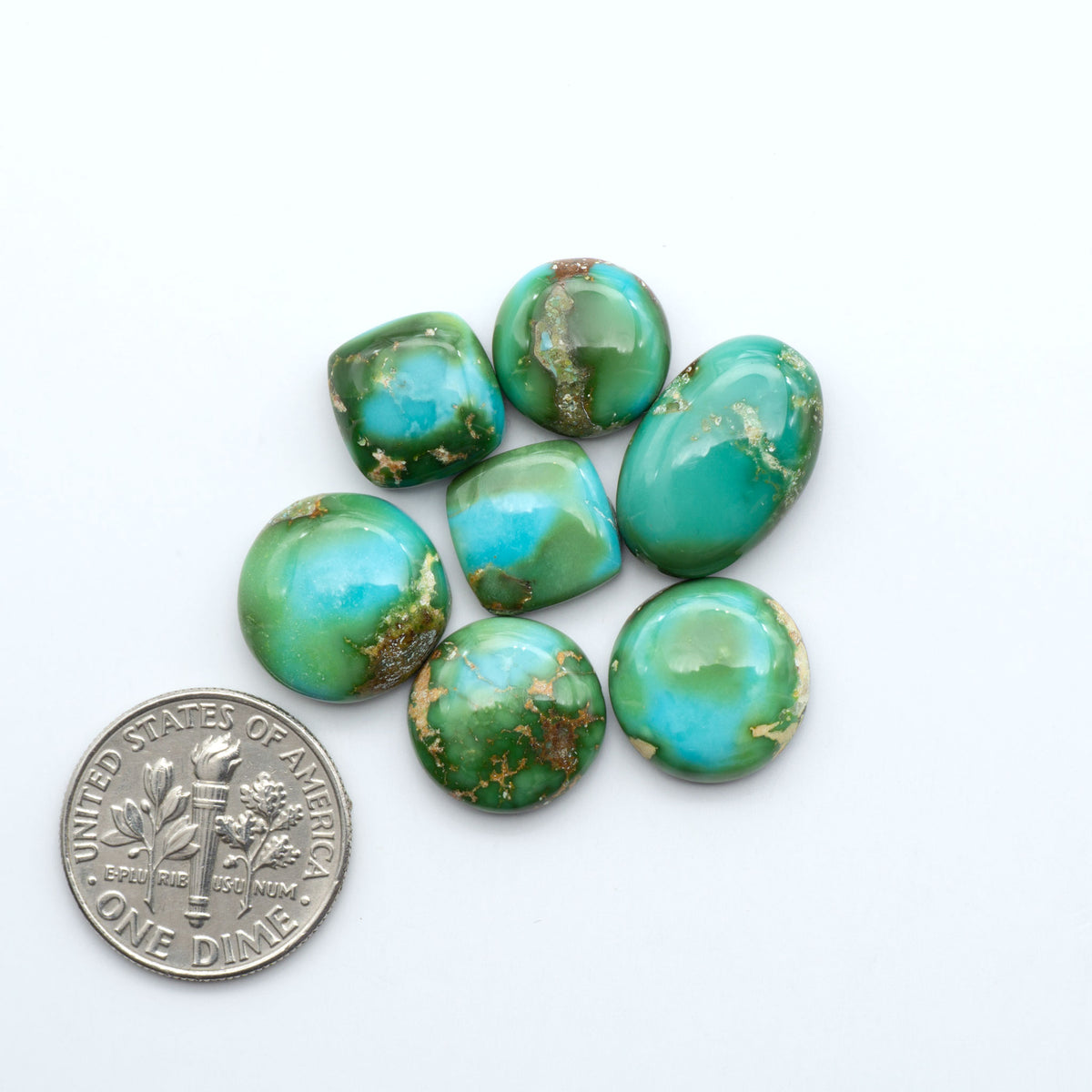 Sonoran Mountain Turquoise cabochons, blue-green color with natural matrix, polished stones on a white background, with a US dime for scale