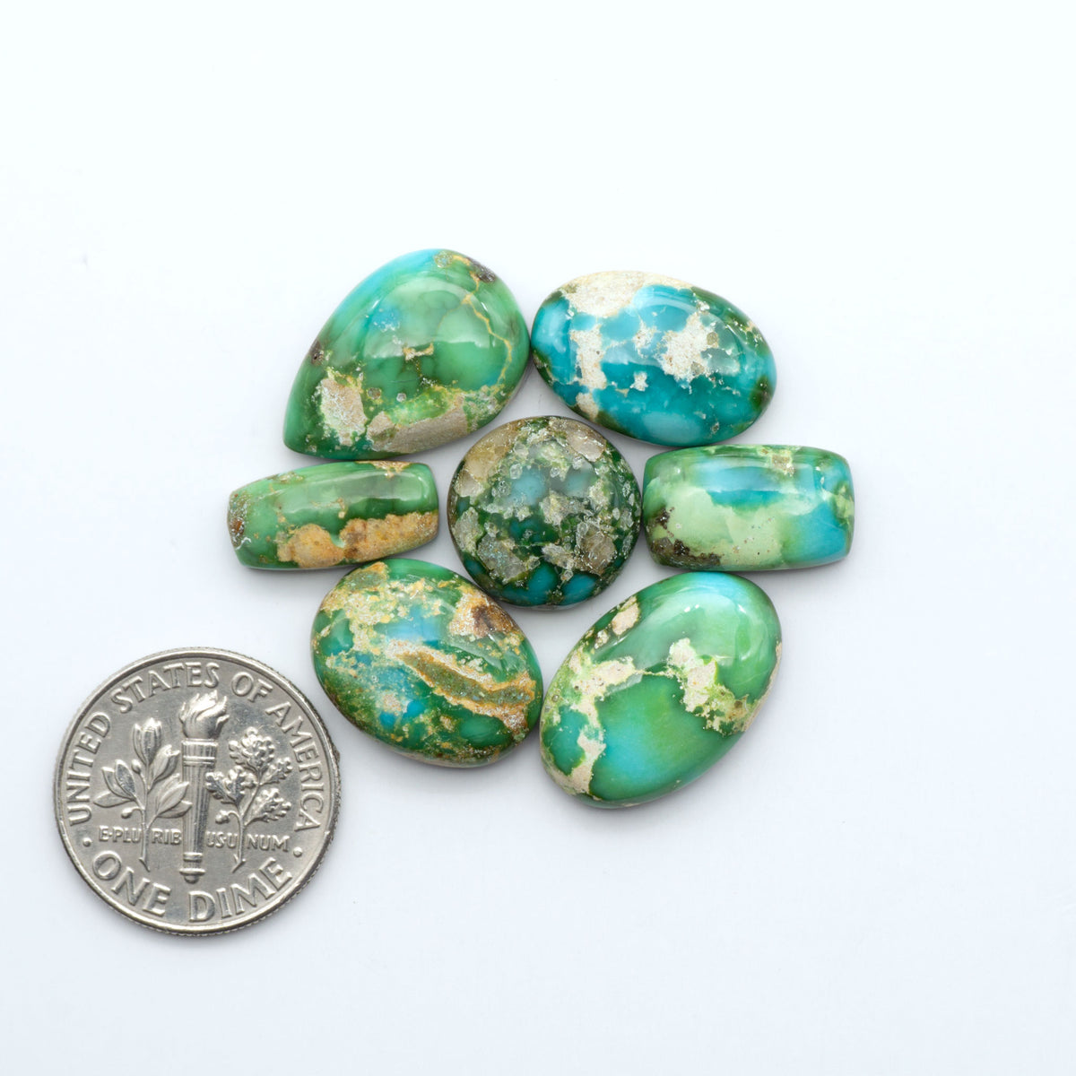 Sonoran Mountain Turquoise cabochons, blue-green color with natural matrix, polished stones on a white background, with a US dime for scale