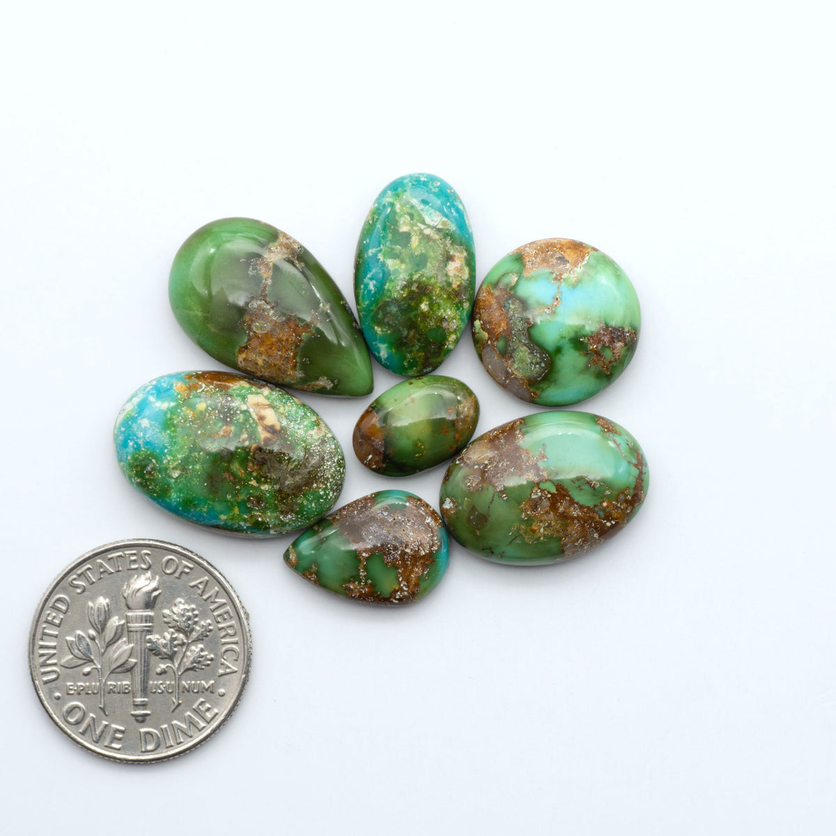 Sonoran Mountain Turquoise cabochons, blue-green color with natural matrix, polished stones on a white background, with a US dime for scale