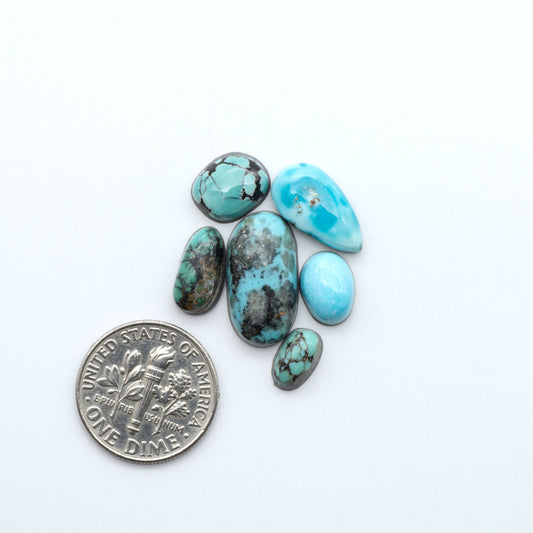 Assorted turquoise cabochon gemstones with varied colors and matrix on a white background with a US dime for scale