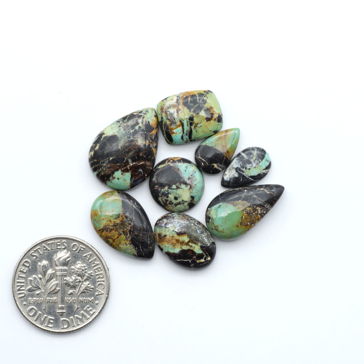 Black Jack turquoise cabochons, blue-green color with black matrix, polished stones on a white background with a US dime for scale