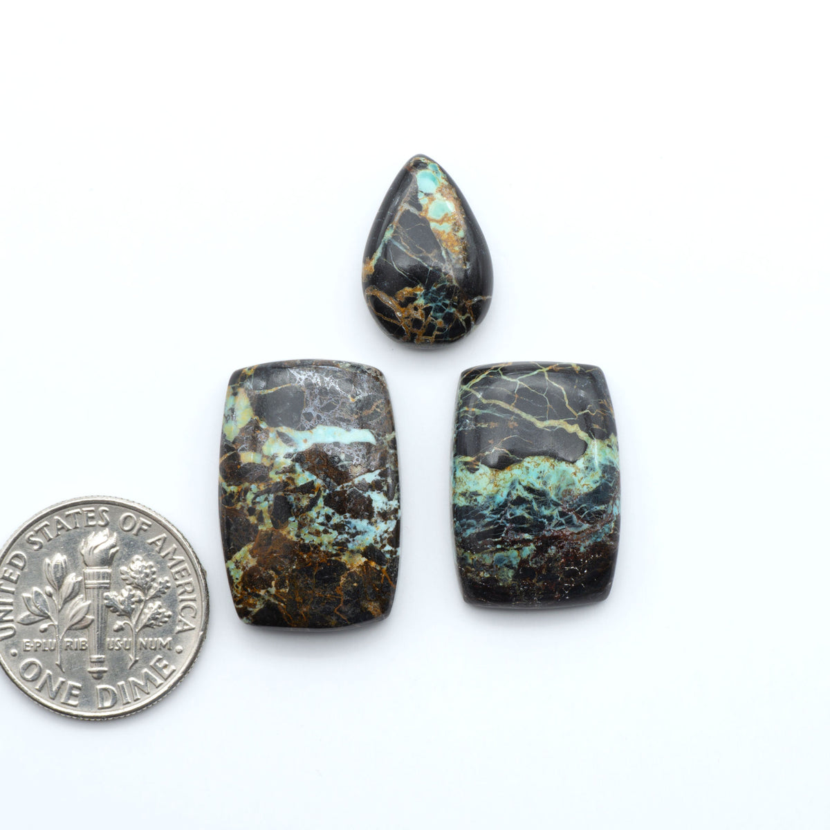 Black Jack turquoise cabochons, blue-green color with black matrix, polished stones on a white background with a US dime for scale