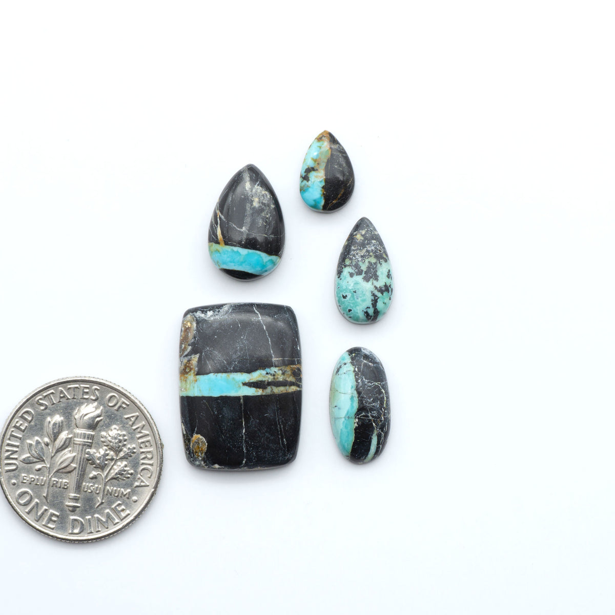 Black Jack turquoise cabochons, blue-green color with black matrix, polished stones on a white background with a US dime for scale