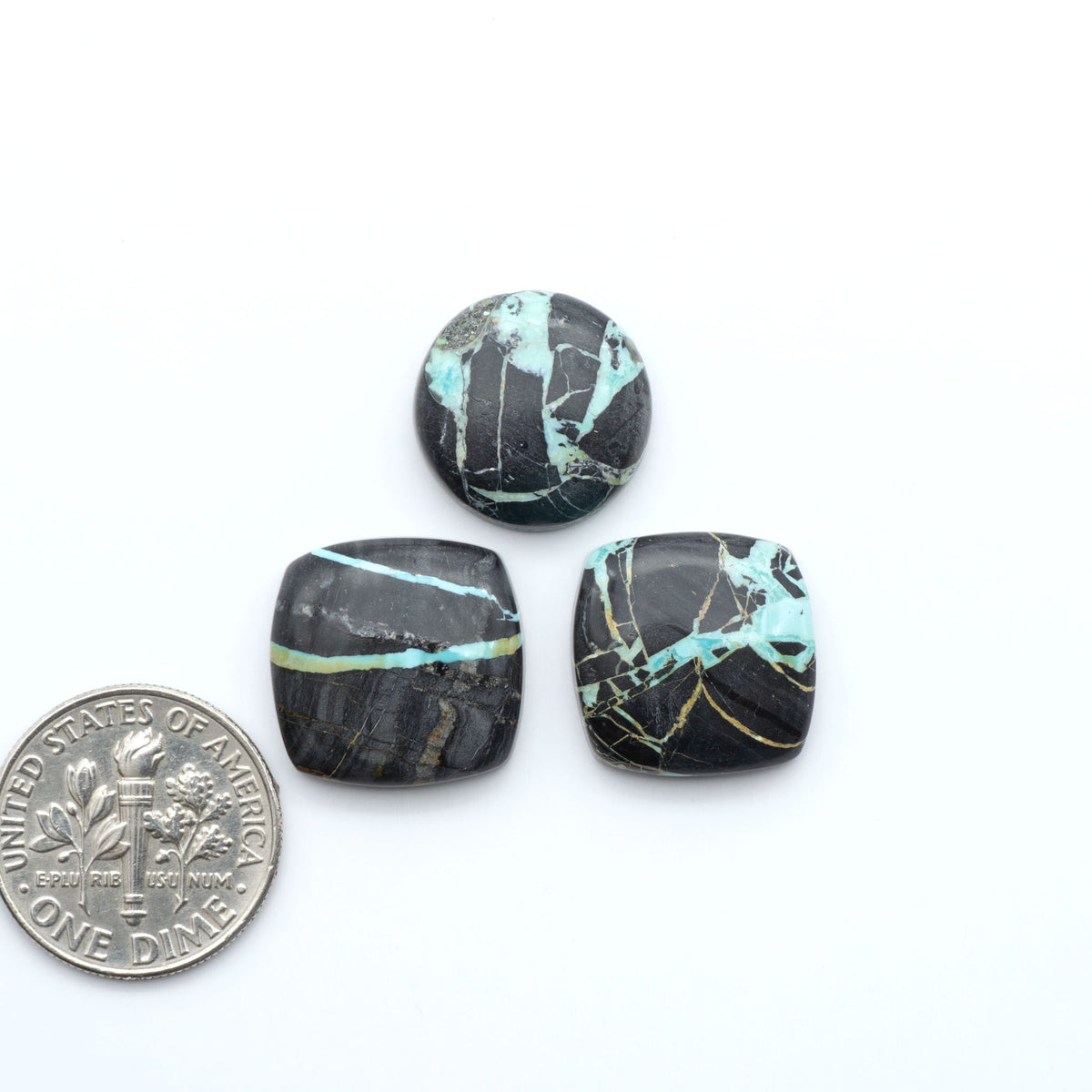Black Jack turquoise cabochons, blue-green color with black matrix, polished stones on a white background with a US dime for scale