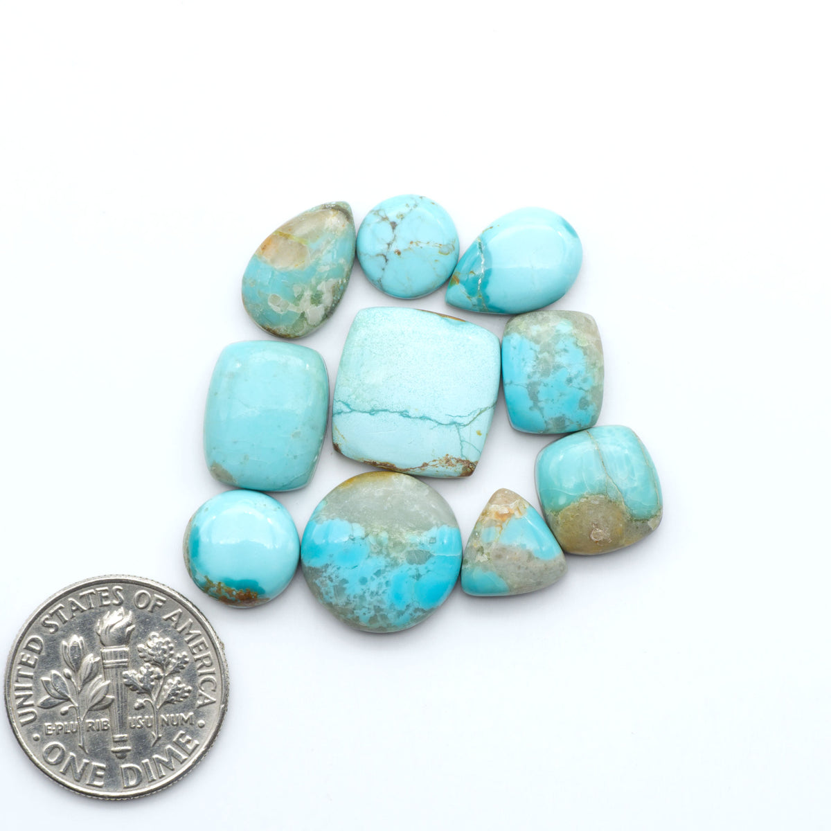 Pilot Mountain Turquoise cabochons, blue-green gemstones with natural matrix on a white background with a US dime for scale
