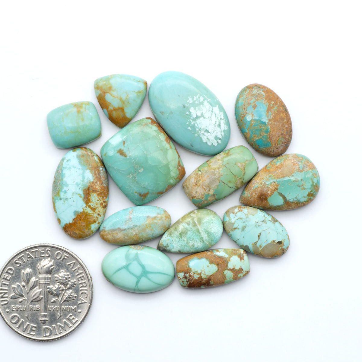 Pilot Mountain Turquoise cabochons, blue-green gemstones with natural matrix on a white background with a US dime for scale