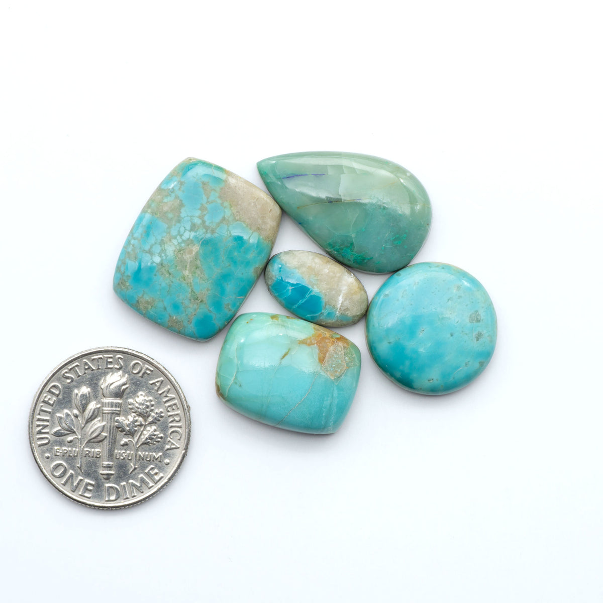 Pilot Mountain Turquoise cabochons, blue-green gemstones with natural matrix on a white background with a US dime for scale