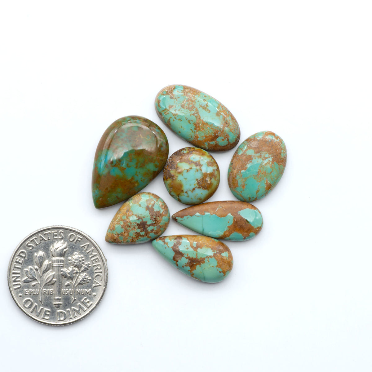Pilot Mountain Turquoise cabochons, blue-green gemstones with natural matrix on a white background with a US dime for scale