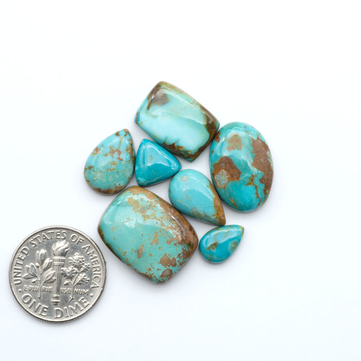 Pilot Mountain Turquoise cabochons, blue-green gemstones with natural matrix on a white background with a US dime for scale