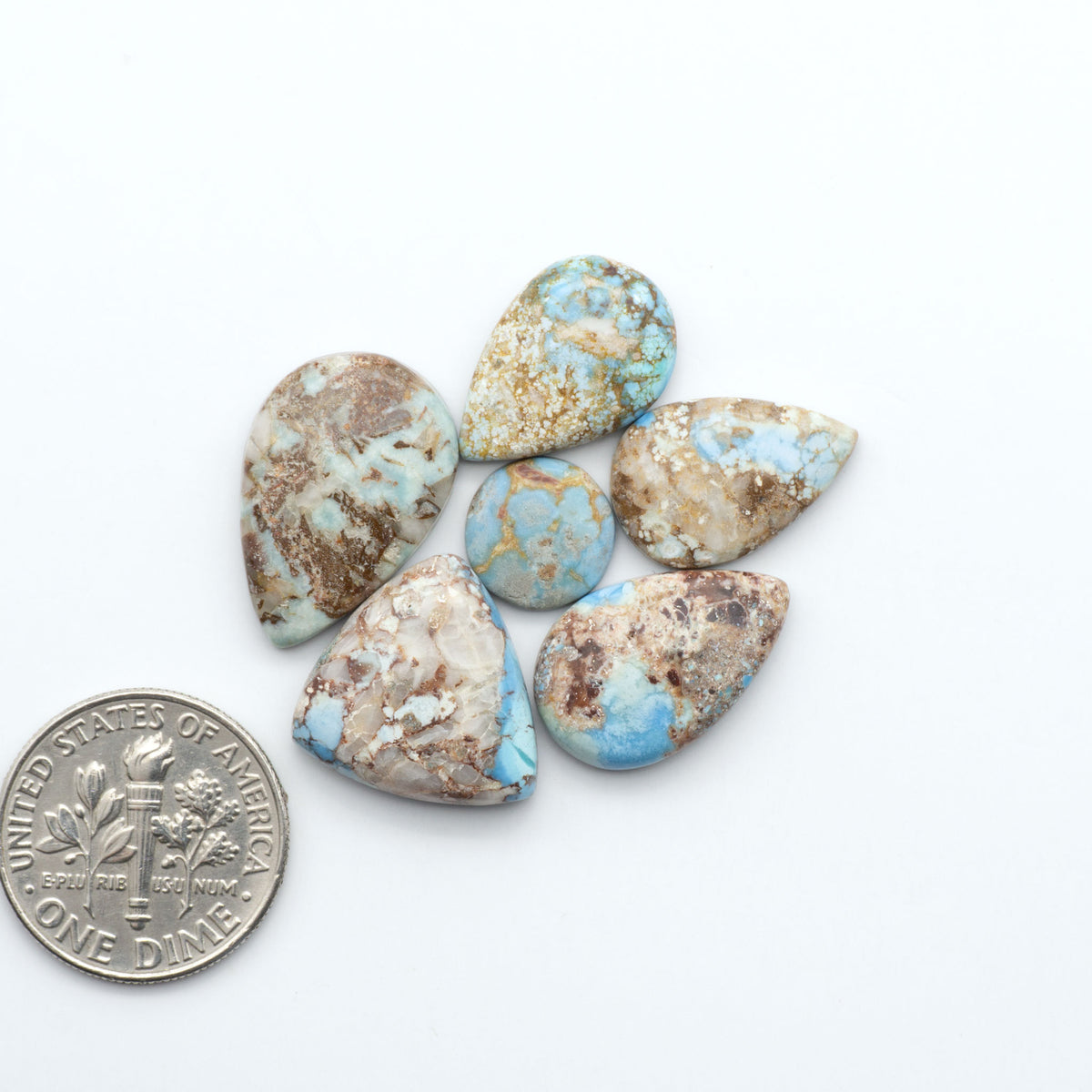 Golden Hills Turquoise cabochons, icy blue to lavender tones with chocolate matrix, polished stones on a white background with a US dime for scale