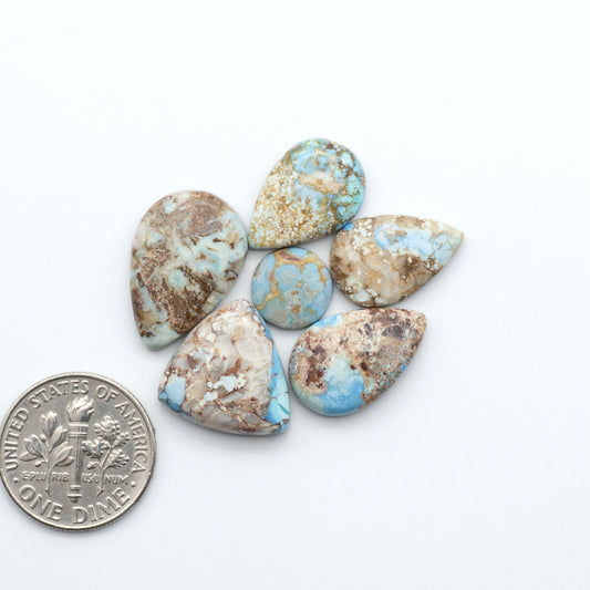 Golden Hills Turquoise cabochons, icy blue to lavender tones with chocolate matrix, polished stones on a white background with a US dime for scale