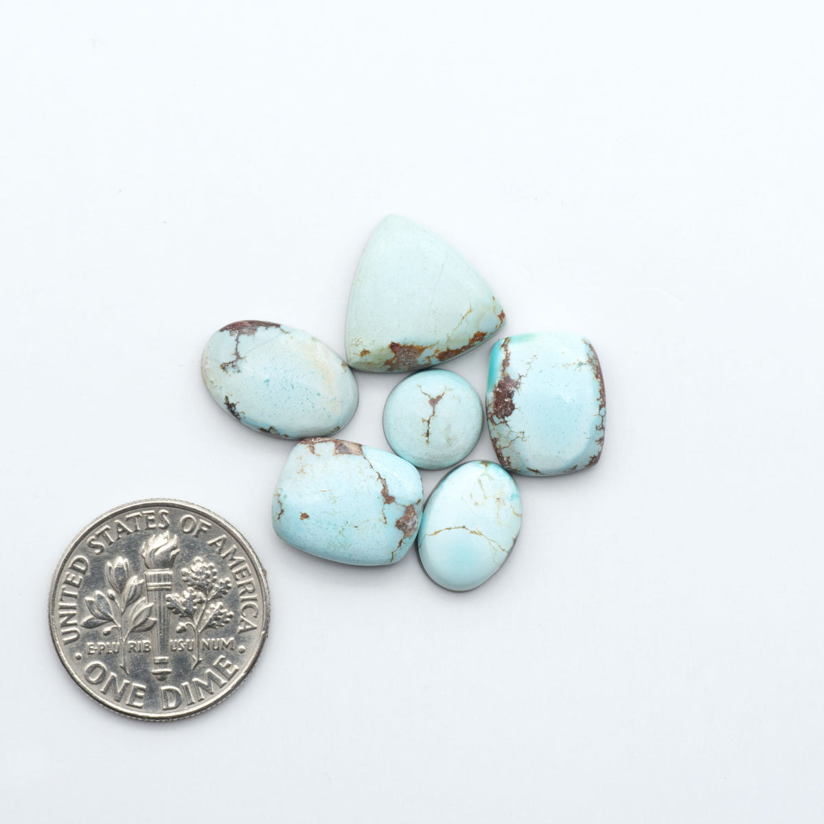Golden Hills Turquoise cabochons, icy blue to lavender tones with chocolate matrix, polished stones on a white background with a US dime for scale