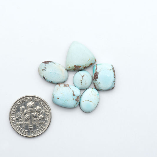Golden Hills Turquoise cabochons, icy blue to lavender tones with chocolate matrix, polished stones on a white background with a US dime for scale