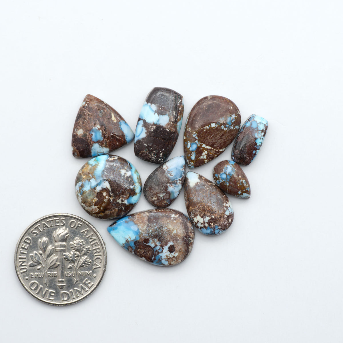 Golden Hills Turquoise cabochons, icy blue to lavender tones with chocolate matrix, polished stones on a white background with a US dime for scale