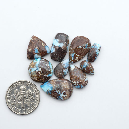 Golden Hills Turquoise cabochons, icy blue to lavender tones with chocolate matrix, polished stones on a white background with a US dime for scale