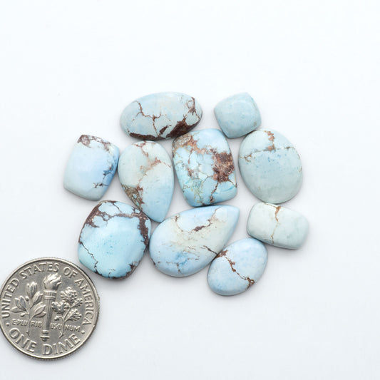 Golden Hills Turquoise cabochons, icy blue to lavender tones with chocolate matrix, polished stones on a white background with a US dime for scale