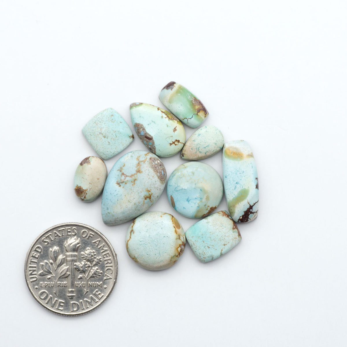 Golden Hills Turquoise cabochons, icy blue to lavender tones with chocolate matrix, polished stones on a white background with a US dime for scale