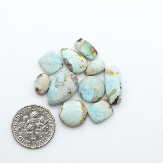 Golden Hills Turquoise cabochons, icy blue to lavender tones with chocolate matrix, polished stones on a white background with a US dime for scale