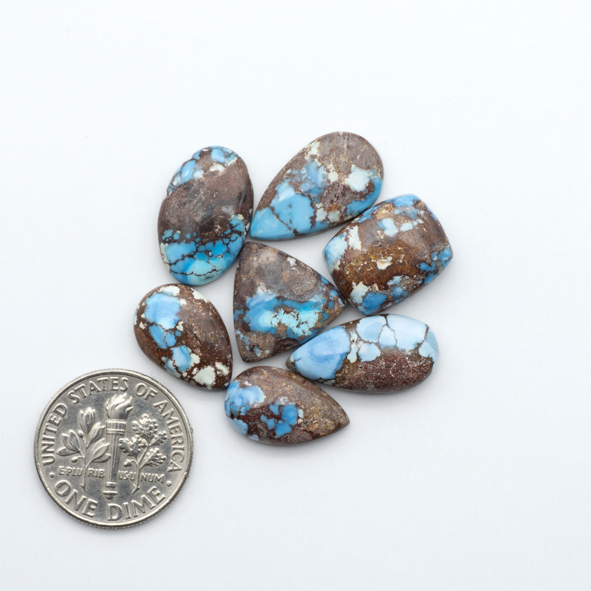 Golden Hills Turquoise cabochons, icy blue to lavender tones with chocolate matrix, polished stones on a white background with a US dime for scale