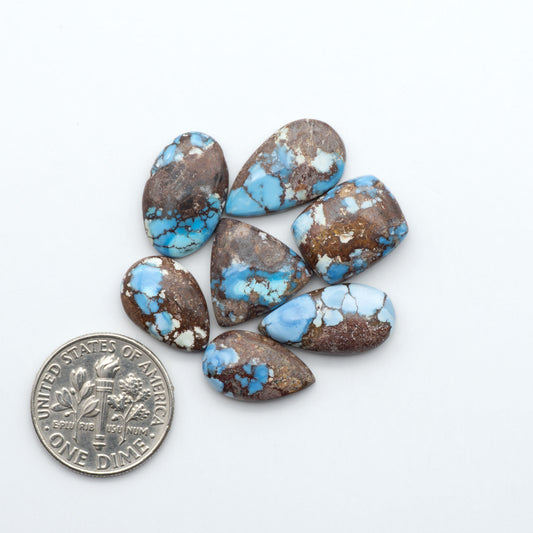 Golden Hills Turquoise cabochons, icy blue to lavender tones with chocolate matrix, polished stones on a white background with a US dime for scale