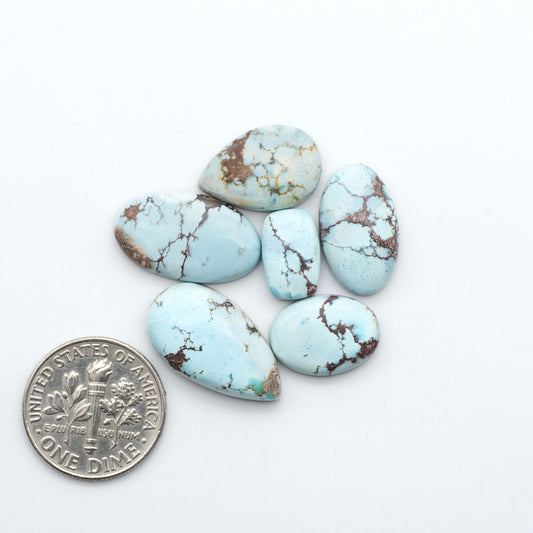 Golden Hills Turquoise cabochons, icy blue to lavender tones with chocolate matrix, polished stones on a white background with a US dime for scale