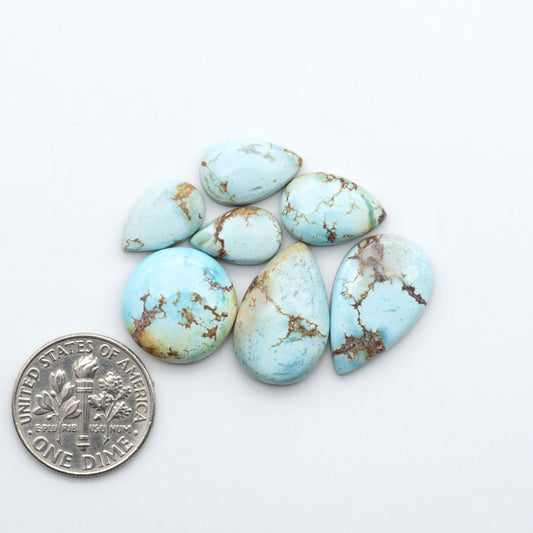 Golden Hills Turquoise cabochons, icy blue to lavender tones with chocolate matrix, polished stones on a white background with a US dime for scale