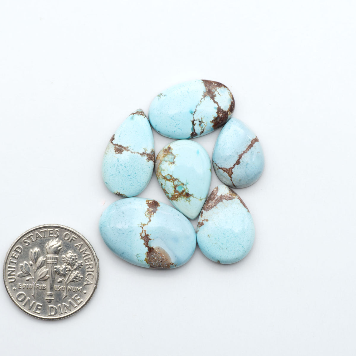 Golden Hills Turquoise cabochons, icy blue to lavender tones with chocolate matrix, polished stones on a white background with a US dime for scale