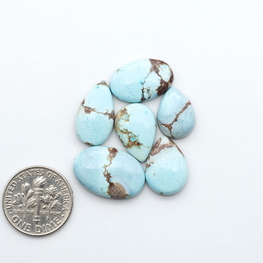 Golden Hills Turquoise cabochons, icy blue to lavender tones with chocolate matrix, polished stones on a white background with a US dime for scale