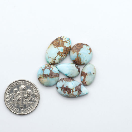 Golden Hills Turquoise cabochons, icy blue to lavender tones with chocolate matrix, polished stones on a white background with a US dime for scale