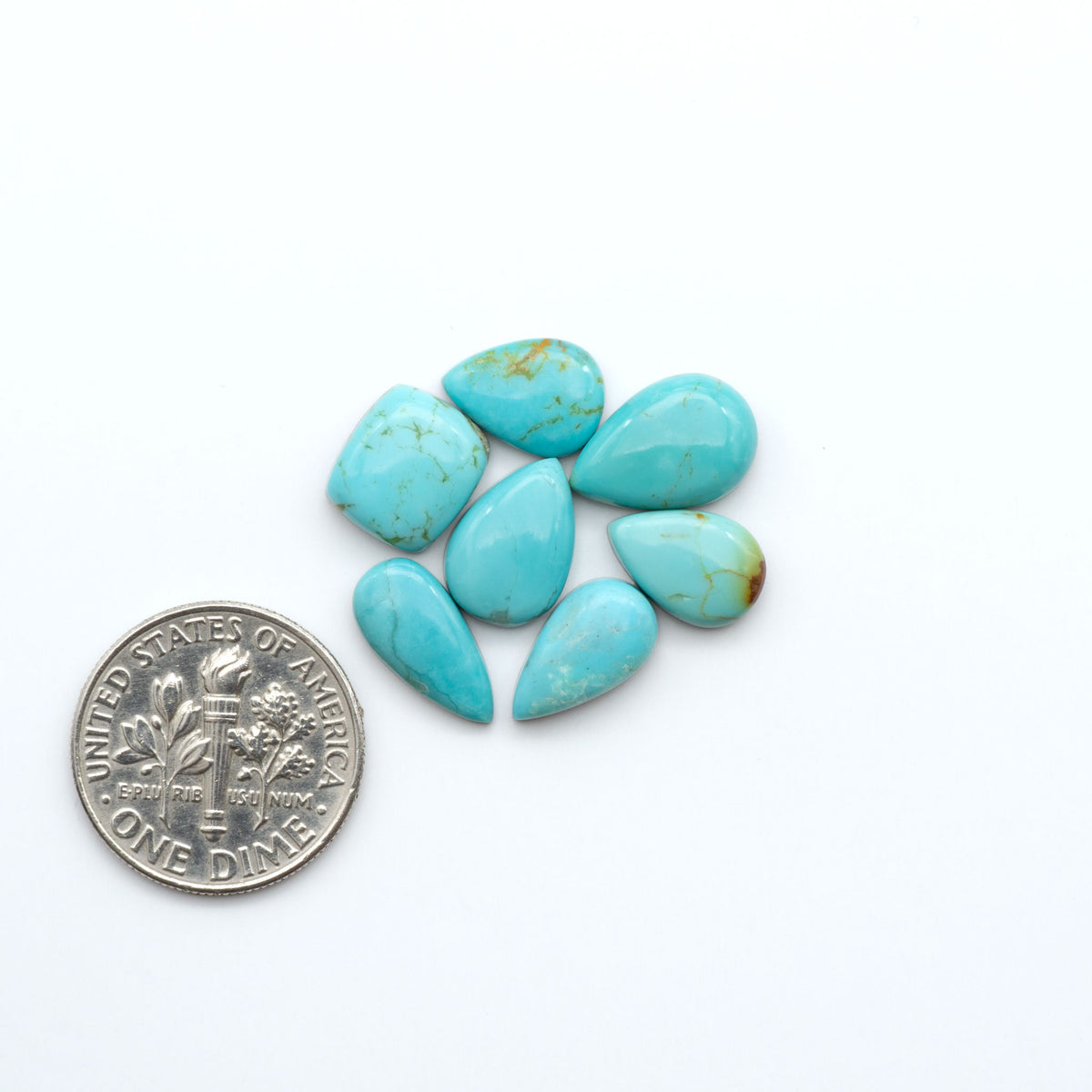 Kings Manassa Turquoise cabochons, polished green-blue gemstones with natural matrix on a white background with a US dime for scale