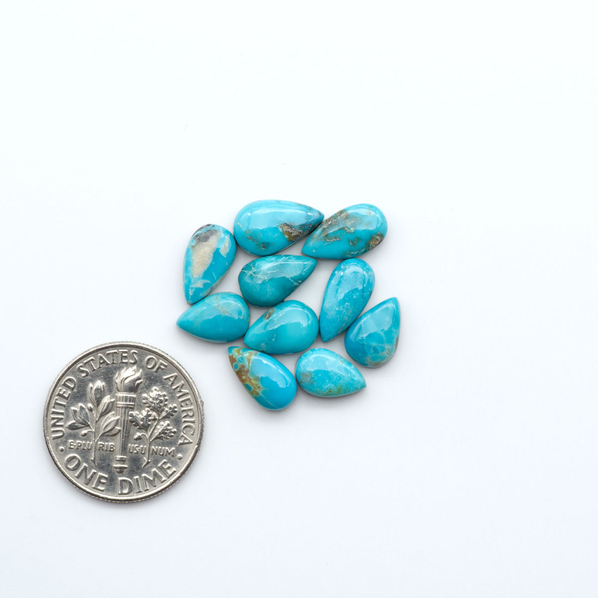 Kings Manassa Turquoise cabochons, polished green-blue gemstones with natural matrix on a white background with a US dime for scale