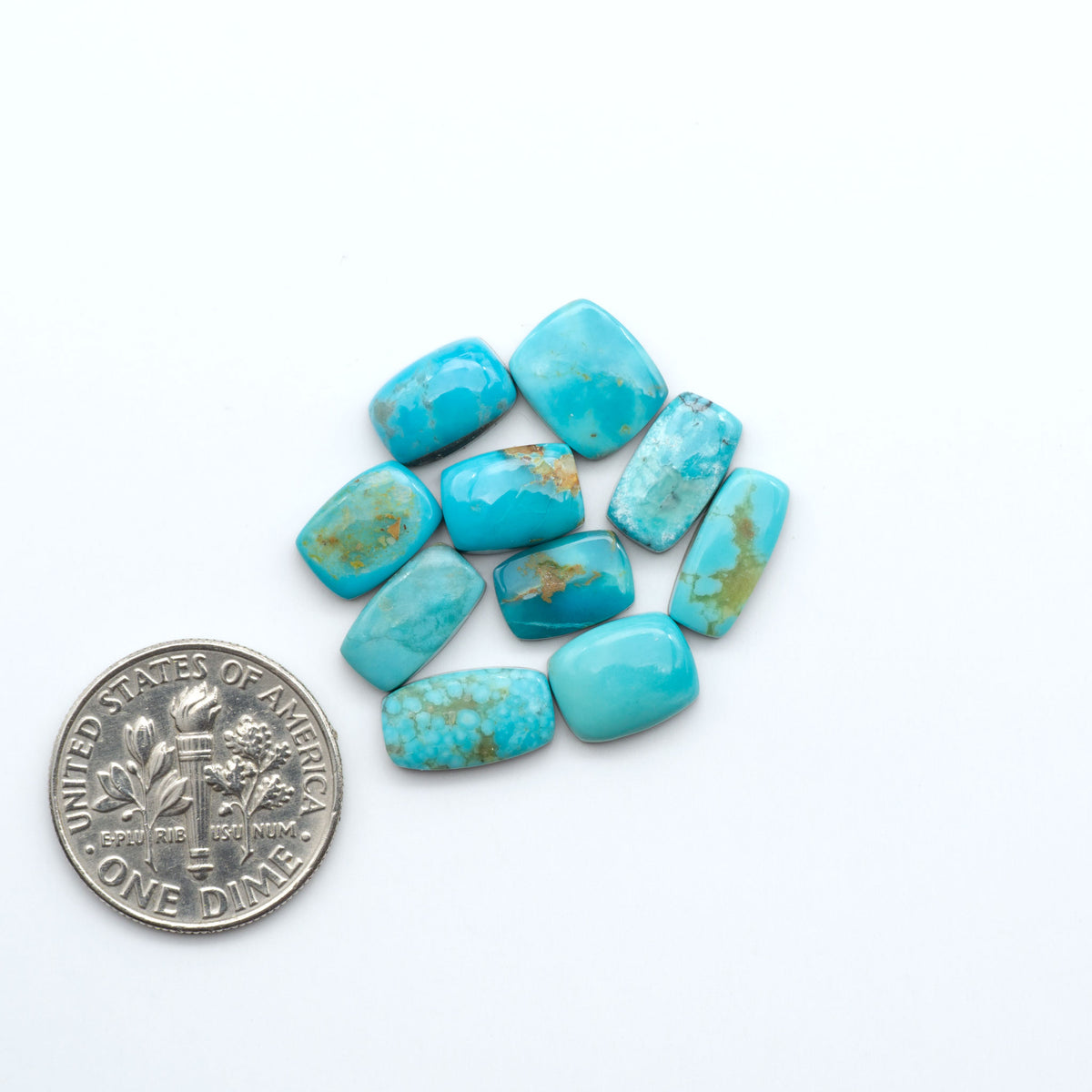 Kings Manassa Turquoise cabochons, polished green-blue gemstones with natural matrix on a white background with a US dime for scale