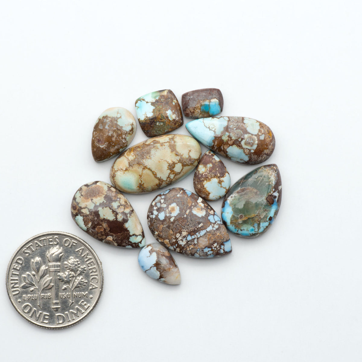 Golden Hills Turquoise cabochons, icy blue to lavender tones with chocolate matrix, polished stones on a white background with a US dime for scale
