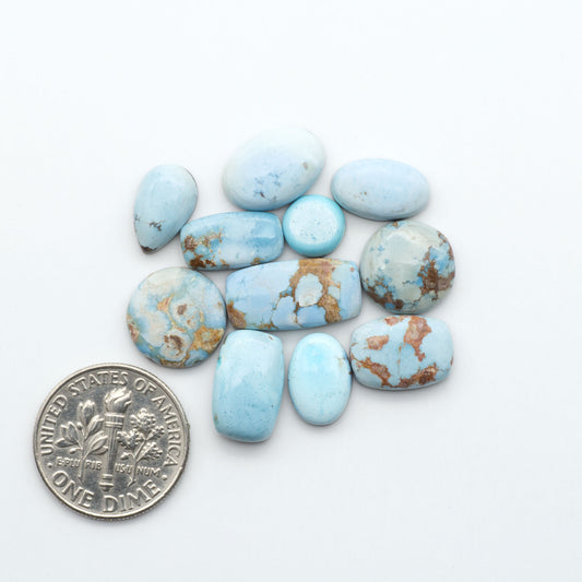 Golden Hills Turquoise cabochons, icy blue to lavender tones with chocolate matrix, polished stones on a white background with a US dime for scale