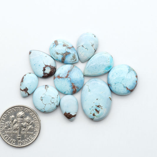 Golden Hills Turquoise cabochons, icy blue to lavender tones with chocolate matrix, polished stones on a white background with a US dime for scale
