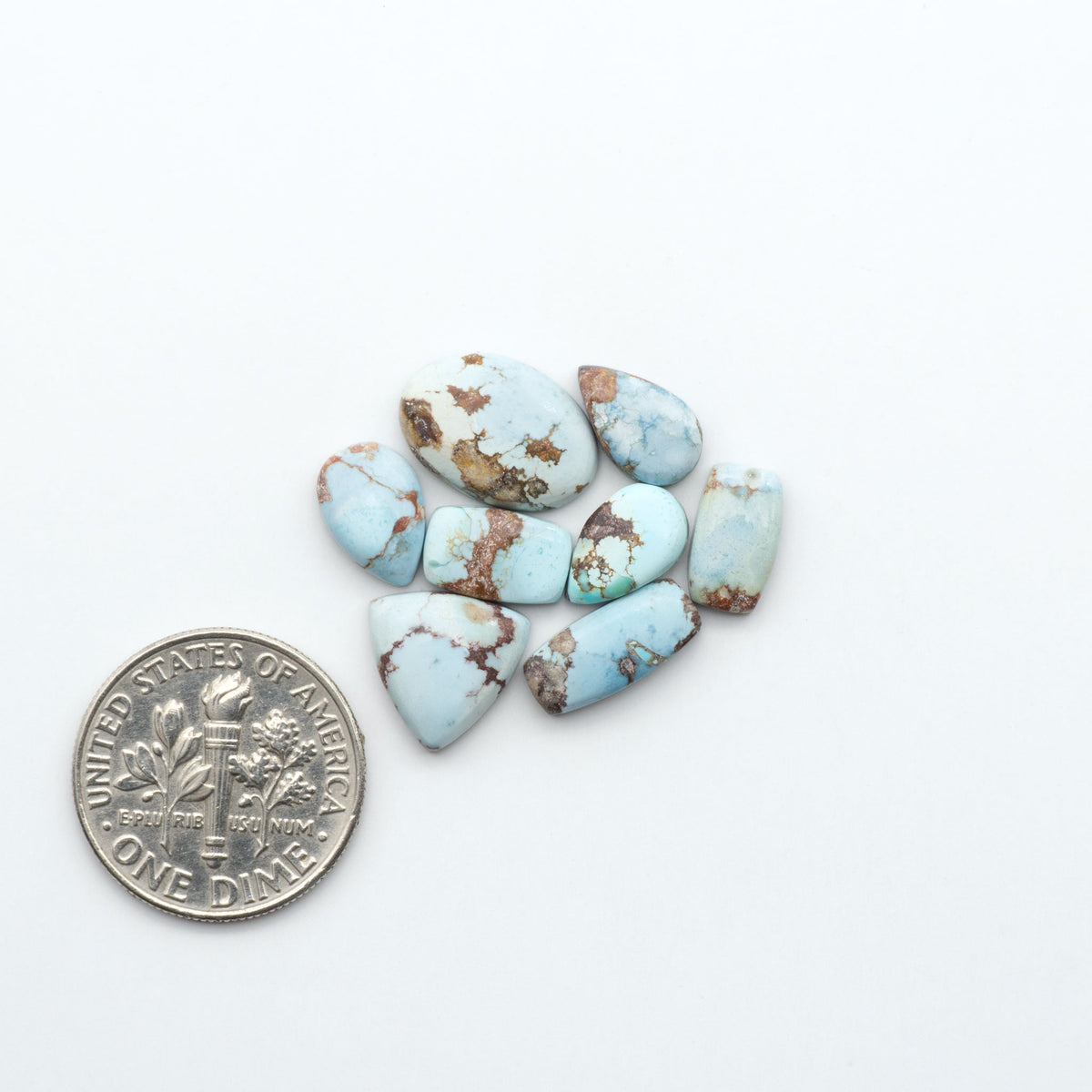 Golden Hills Turquoise cabochons, icy blue to lavender tones with chocolate matrix, polished stones on a white background with a US dime for scale