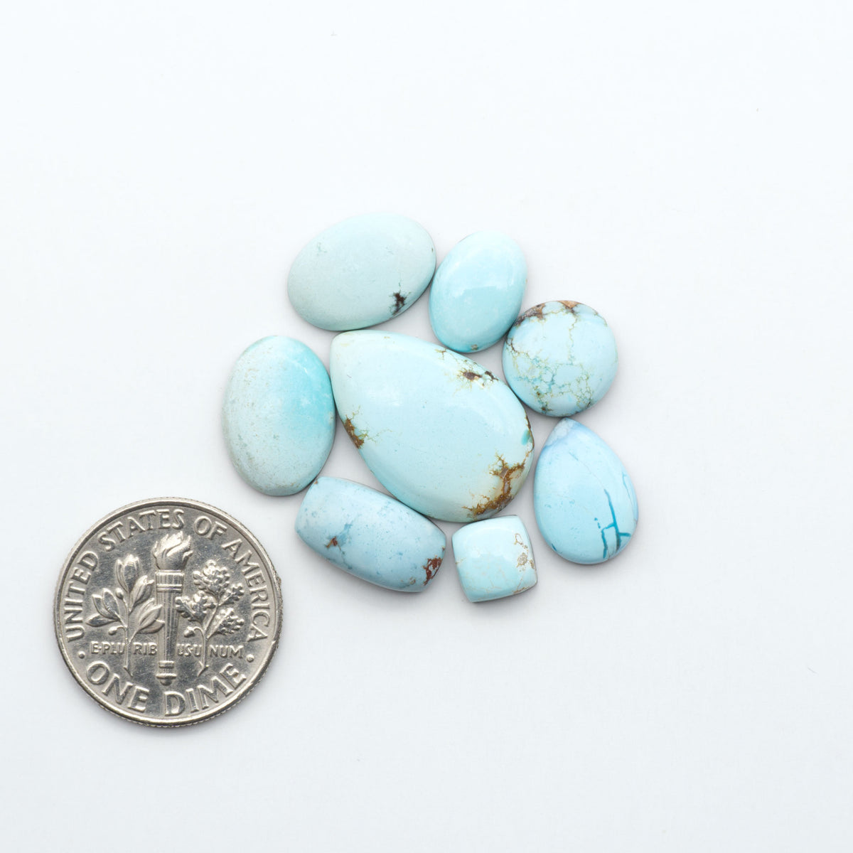 Golden Hills Turquoise cabochons, icy blue to lavender tones with chocolate matrix, polished stones on a white background with a US dime for scale