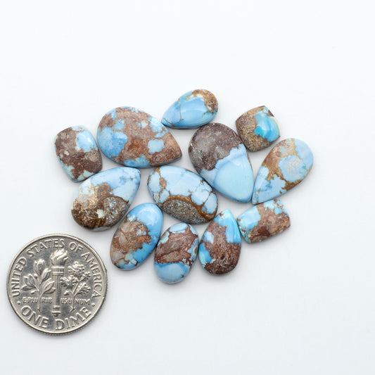 Golden Hills Turquoise cabochons, icy blue to lavender tones with chocolate matrix, polished stones on a white background with a US dime for scale