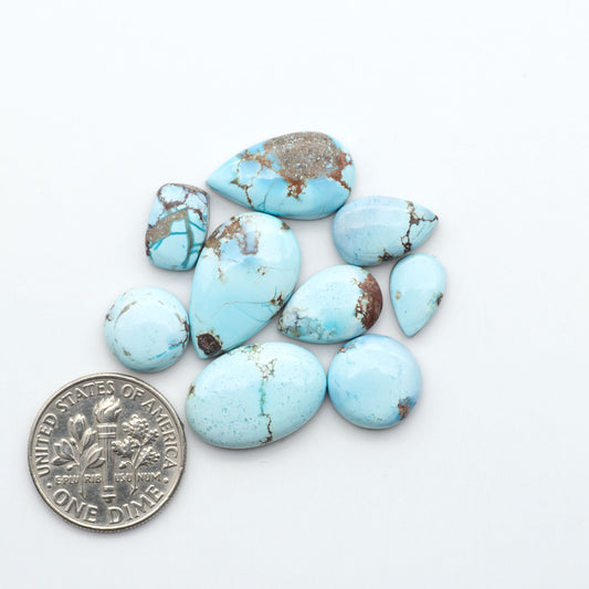 Golden Hills Turquoise cabochons, icy blue to lavender tones with chocolate matrix, polished stones on a white background with a US dime for scale