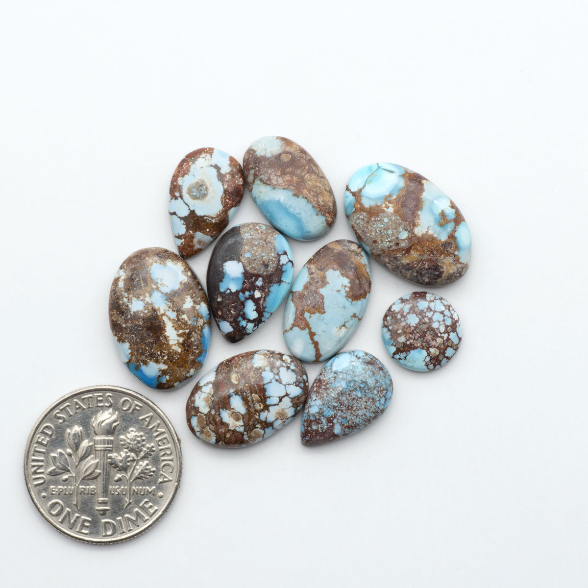 Golden Hills Turquoise cabochons, icy blue to lavender tones with chocolate matrix, polished stones on a white background with a US dime for scale