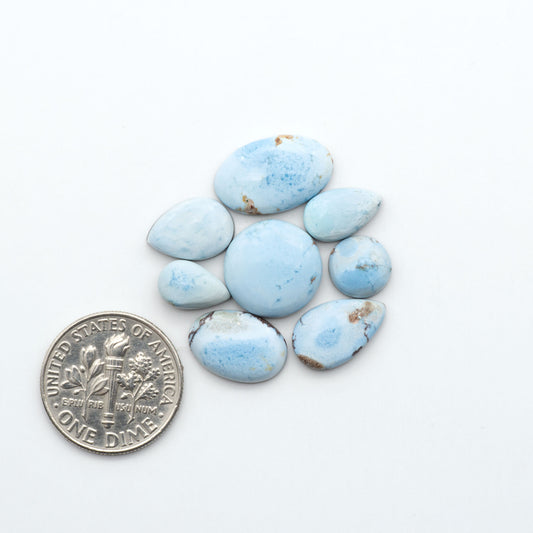 Golden Hills Turquoise cabochons, icy blue to lavender tones with chocolate matrix, polished stones on a white background with a US dime for scale