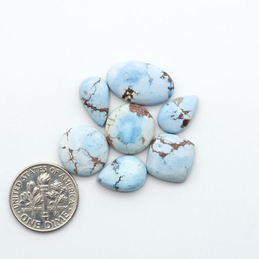 Golden Hills Turquoise cabochons, icy blue to lavender tones with chocolate matrix, polished stones on a white background with a US dime for scale