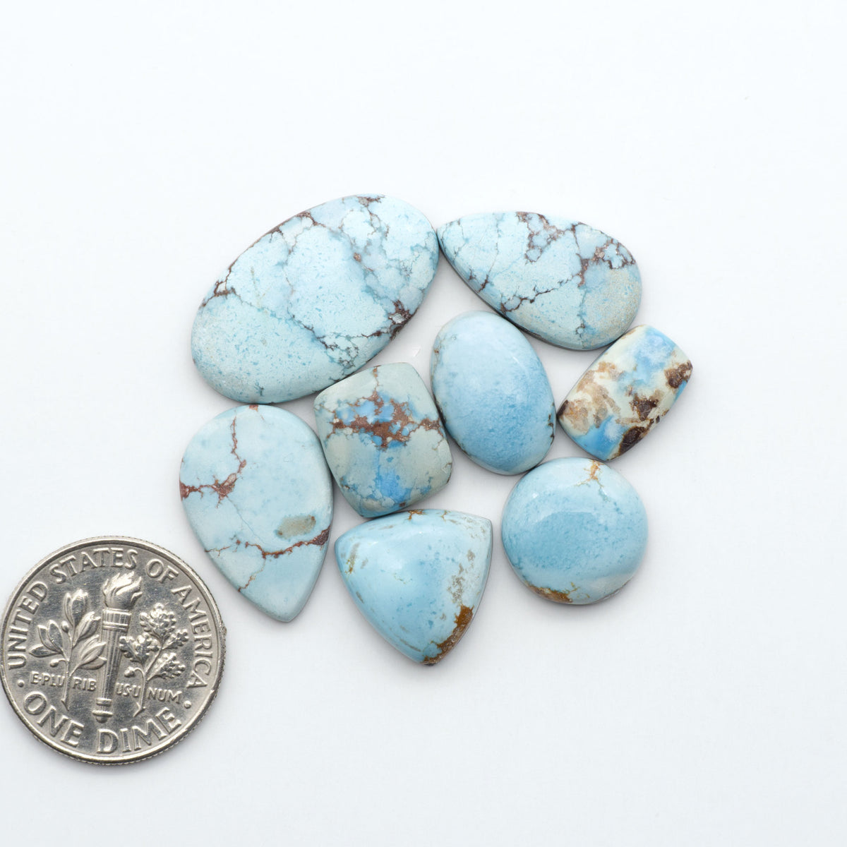 Golden Hills Turquoise cabochons, icy blue to lavender tones with chocolate matrix, polished stones on a white background with a US dime for scale
