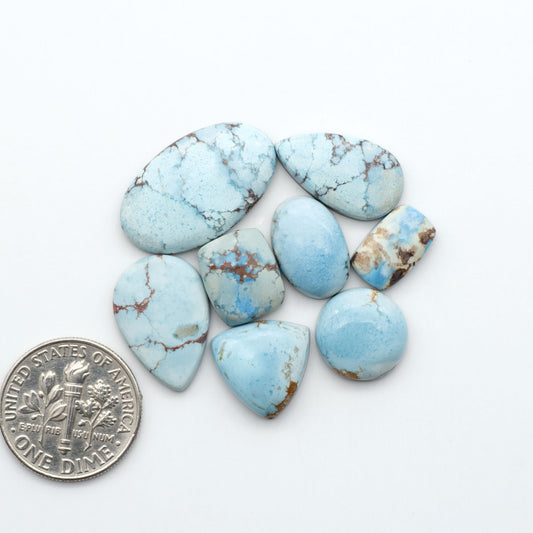 Golden Hills Turquoise cabochons, icy blue to lavender tones with chocolate matrix, polished stones on a white background with a US dime for scale