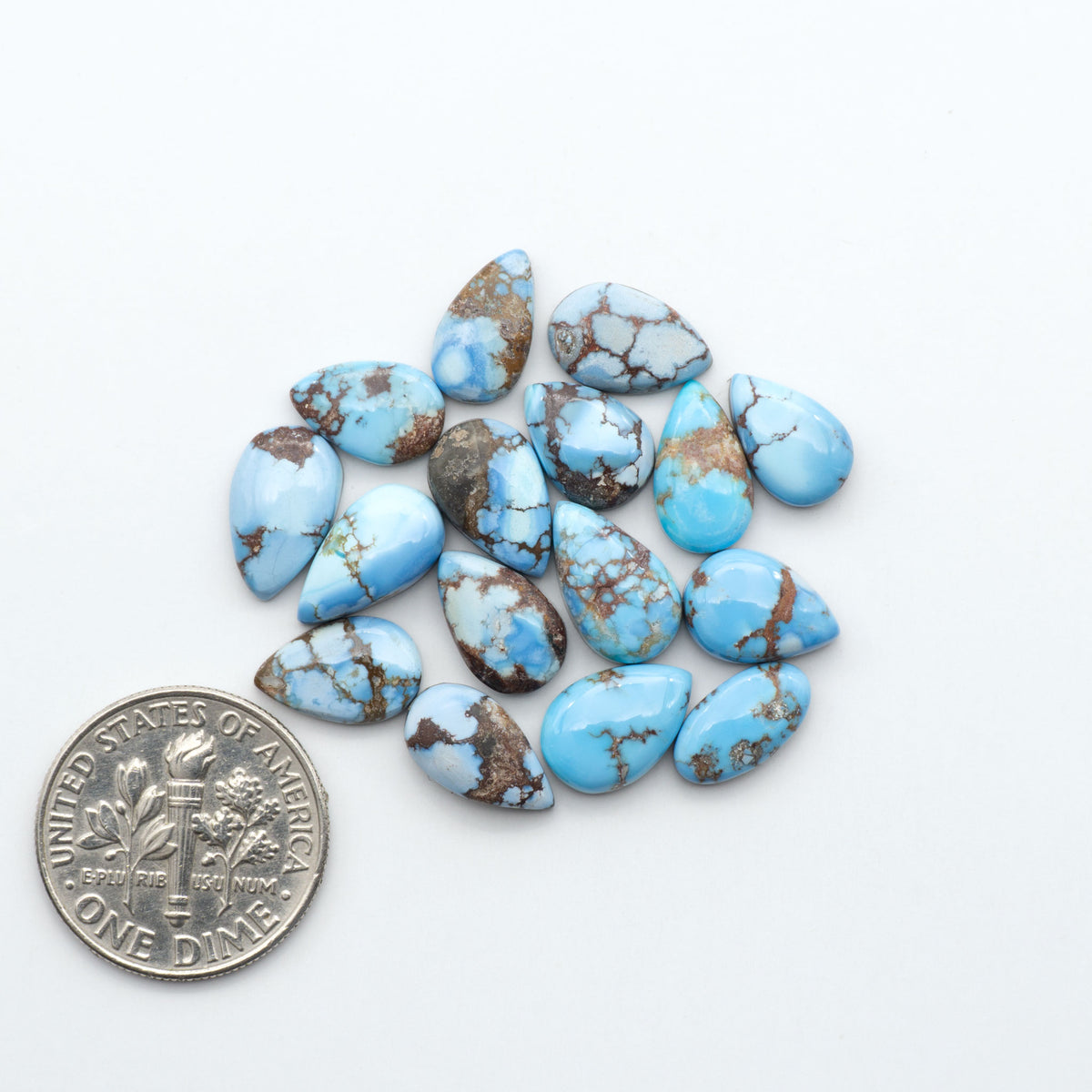 Golden Hills Turquoise cabochons, icy blue to lavender tones with chocolate matrix, polished stones on a white background with a US dime for scale