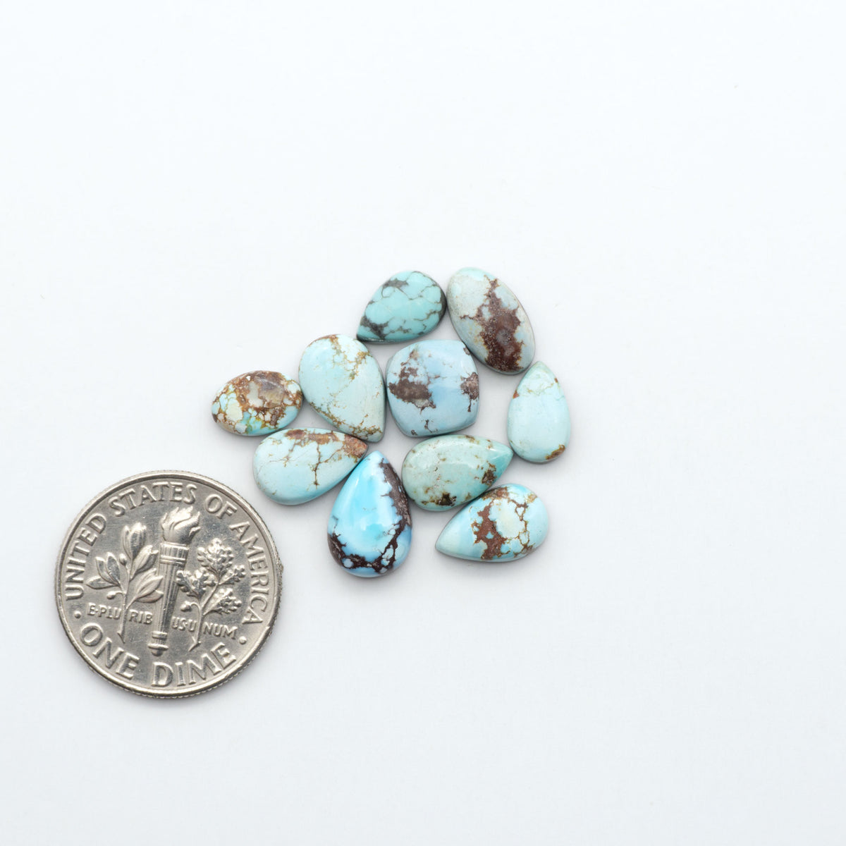 Golden Hills Turquoise cabochons, icy blue to lavender tones with chocolate matrix, polished stones on a white background with a US dime for scale