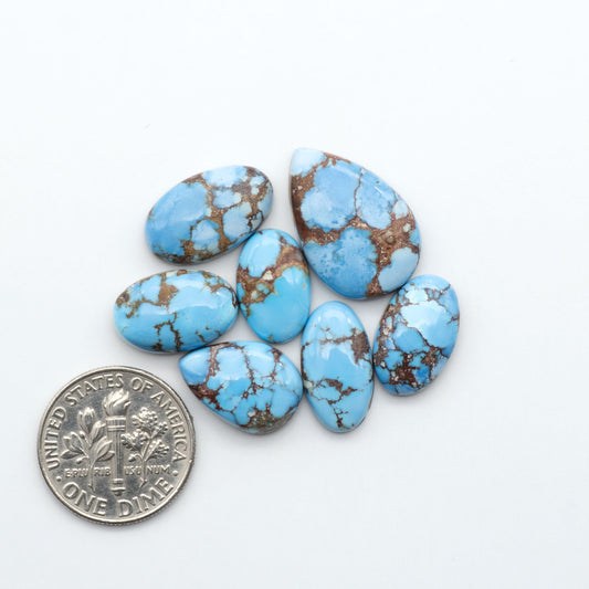 Golden Hills Turquoise cabochons, icy blue to lavender tones with chocolate matrix, polished stones on a white background with a US dime for scale
